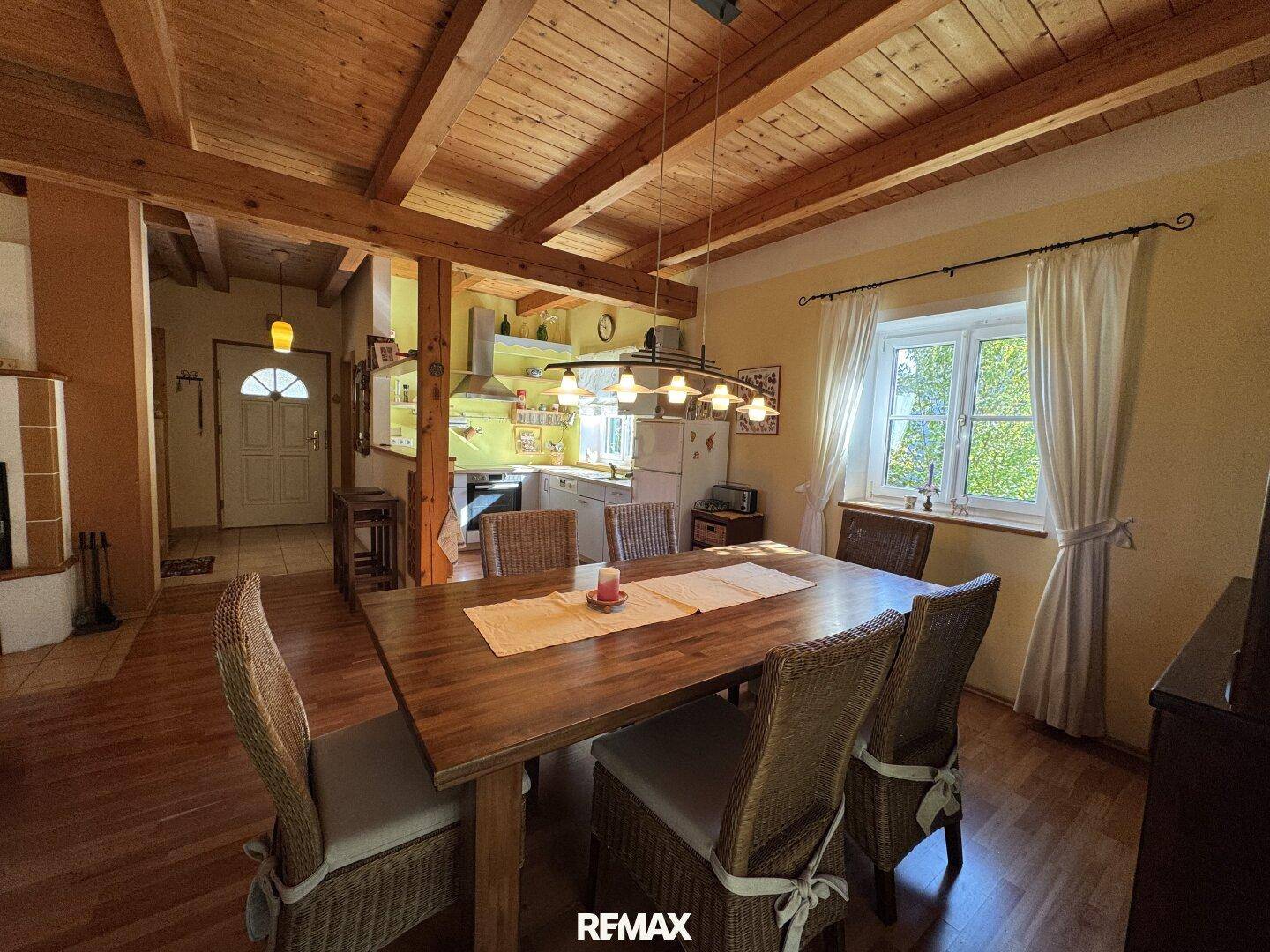 Gemütlicher Essbereich mit Holztisch und Stühlen, offen zur Küche, unter einer rustikalen Holzdecke.