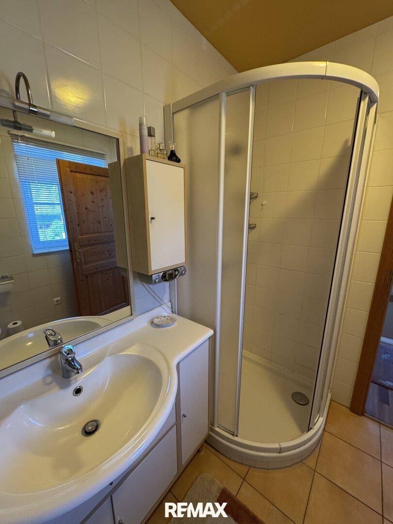 Detailansicht des Badezimmers mit Waschtisch, Spiegelschrank und einer Eckdusche.
