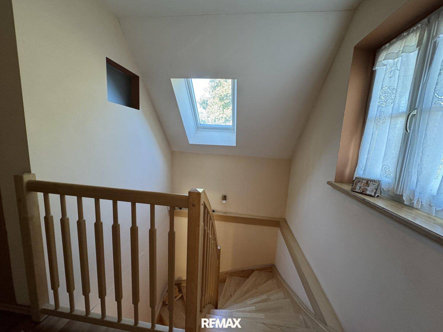 Holztreppe mit natürlichem Lichteinfall durch ein Dachfenster und ein Seitenfenster.