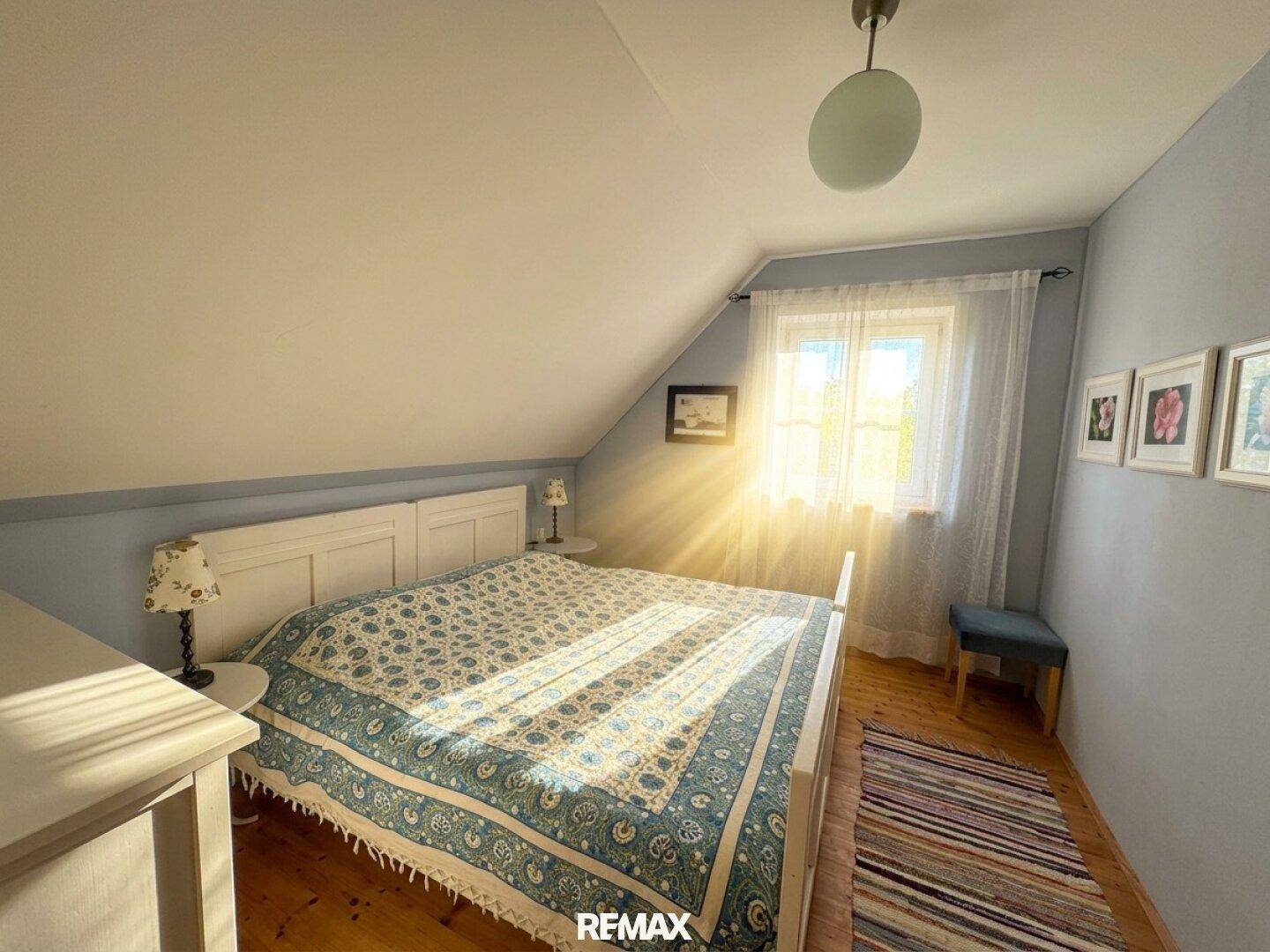 Helles Schlafzimmer mit Doppelbett, Dachschräge und viel Sonnenlicht durch das Fenster.