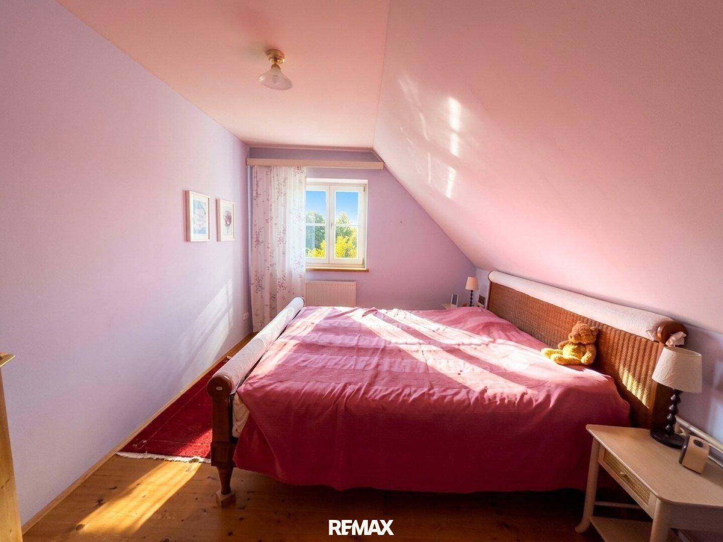 Gemütliches Schlafzimmer mit Doppelbett, Dachschräge und Fenster, in sanften Rosatönen gehalten.
