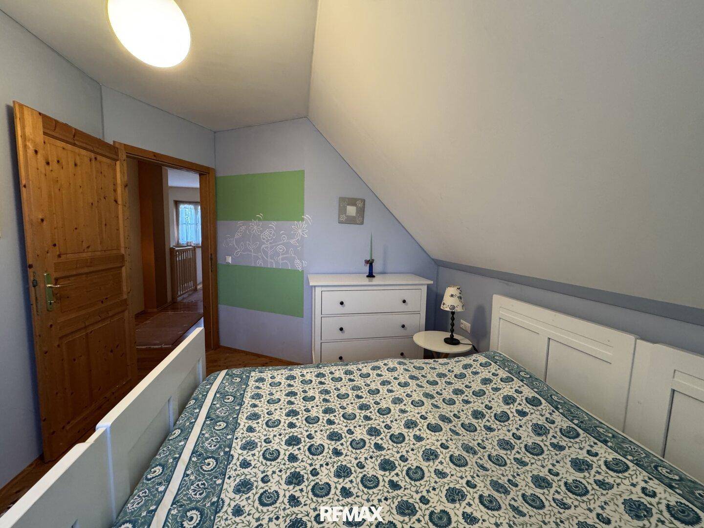 Schlafzimmer mit Doppelbett und Kommode, die Tür führt zu einem angrenzenden Flur.