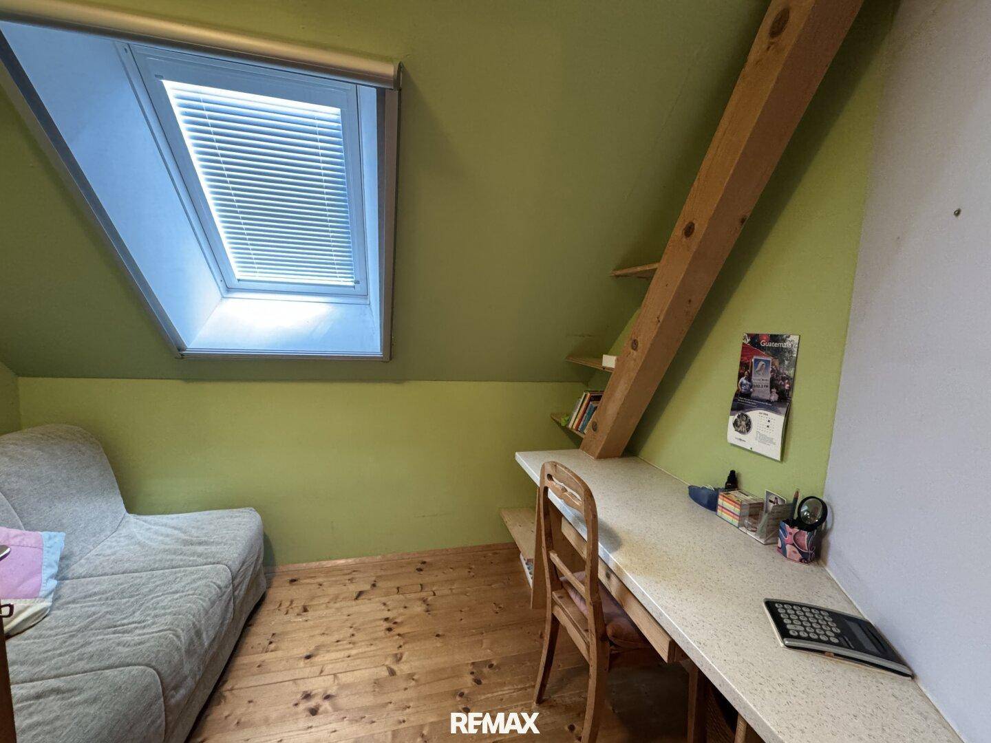 Arbeitszimmer mit Schreibtisch, Sofa und Dachfenster, das für natürliches Licht sorgt.