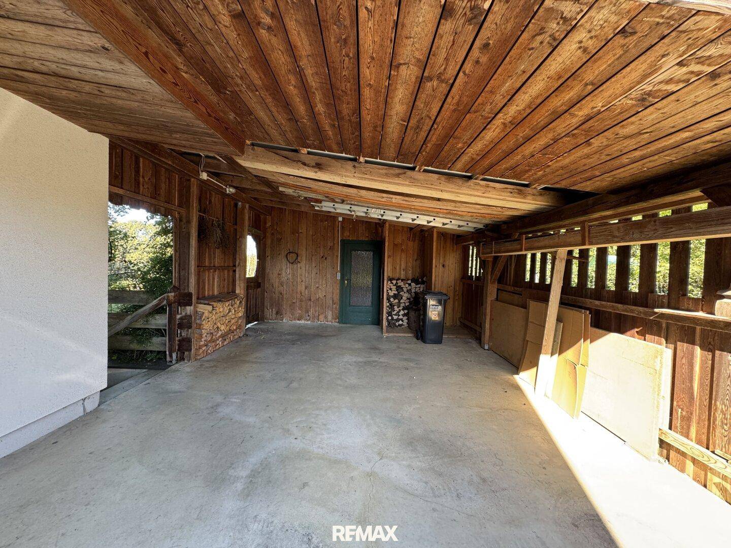 Überdachter Bereich mit Holzwänden und Betonboden, ideal als Carport oder Lagerfläche.