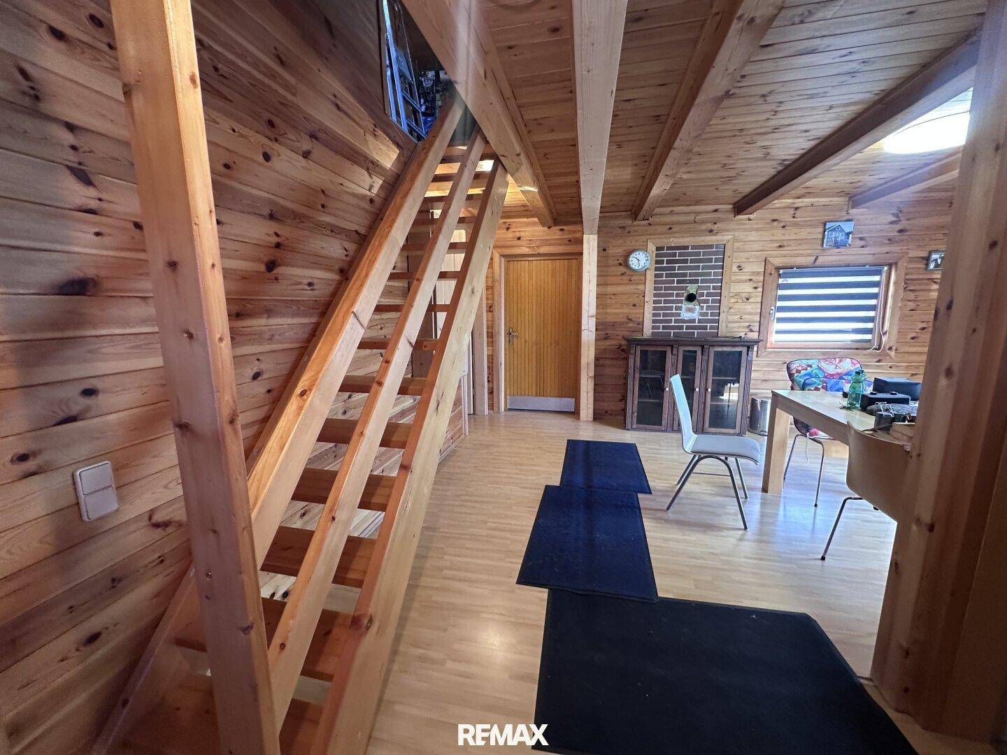 Offener Wohnbereich mit Holztreppe zum Obergeschoss und rustikaler Holztäfelung.