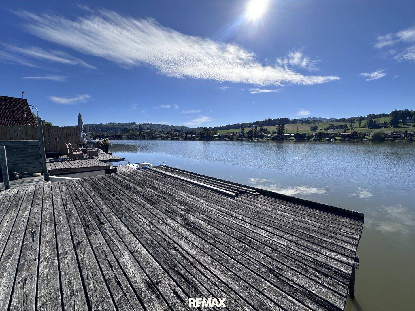 Weitläufiger Blick über den See mit einem langen Holzsteg unter strahlend blauem Himmel.