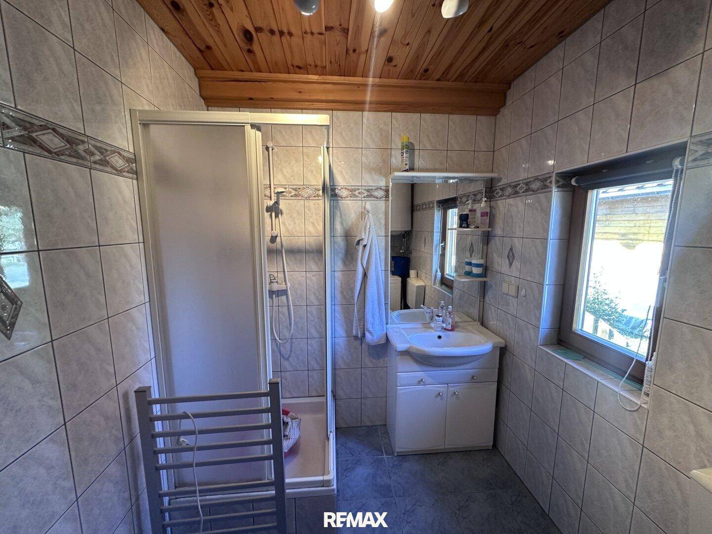 Funktionales Badezimmer mit Fliesen, Duschkabine, Einzelwaschbecken und Holzdecke.