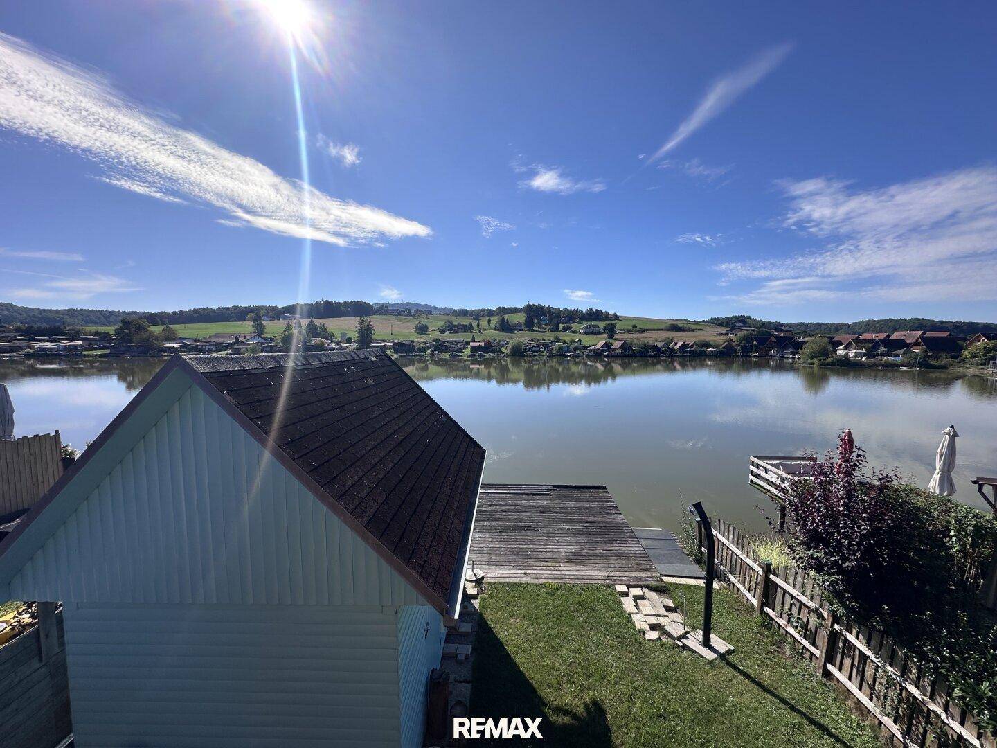 Panoramablick über den See und die umliegende Landschaft, mit dem Holzsteg im Vordergrund.