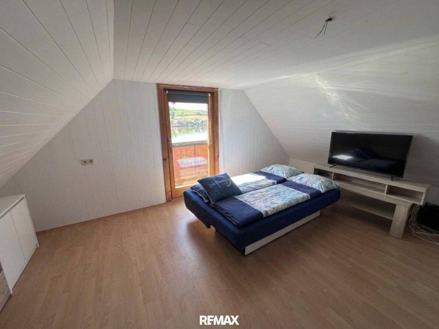 Gemütliches Schlafzimmer im Dachgeschoss mit schrägen Wänden, Laminatboden und Seeblick vom Balkon.