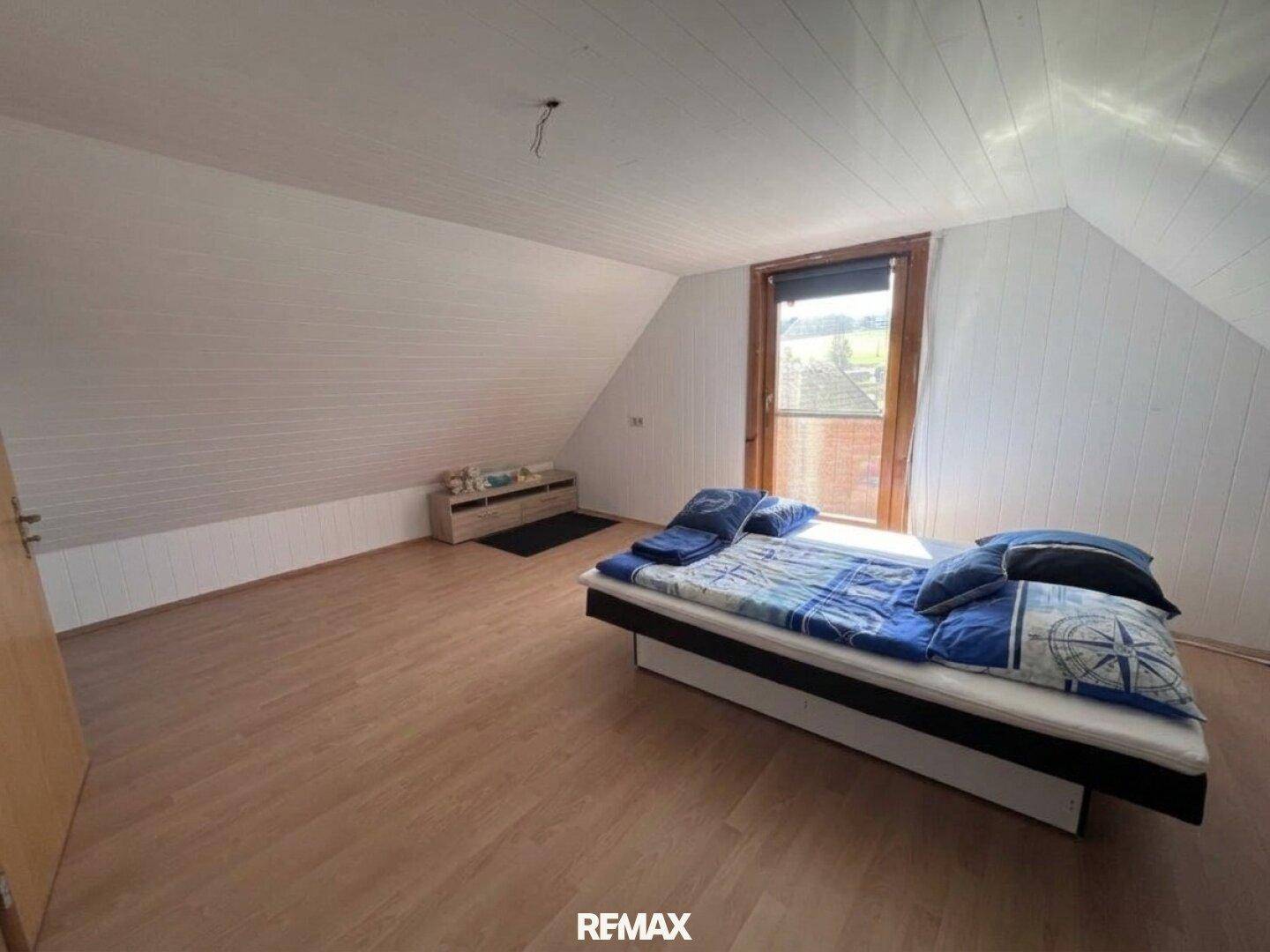 Helles Dachgeschoss-Schlafzimmer mit weiß getäfelten Wänden und Laminatboden, bietet viel Platz.