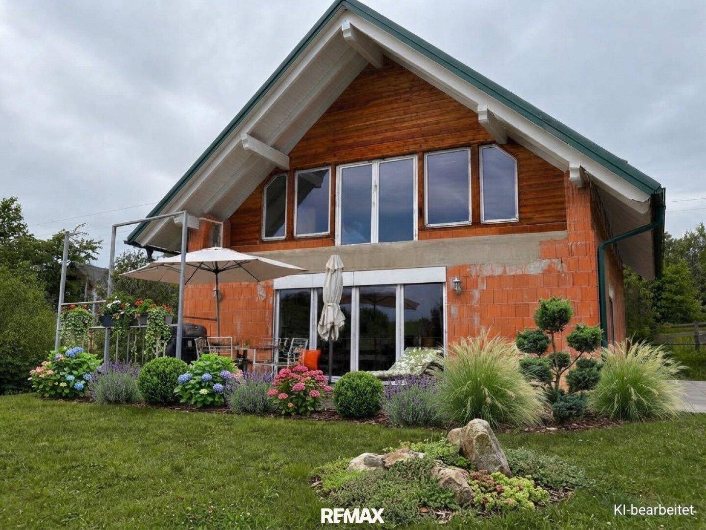 Rückseite des Hauses mit gepflegtem Garten, blühenden Pflanzen und einer kleinen Terrasse.