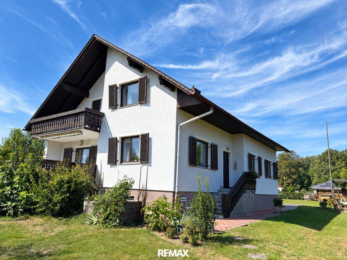 Seitenansicht des Hauses mit weißer Fassade, braunen Fensterläden und Außentreppe.