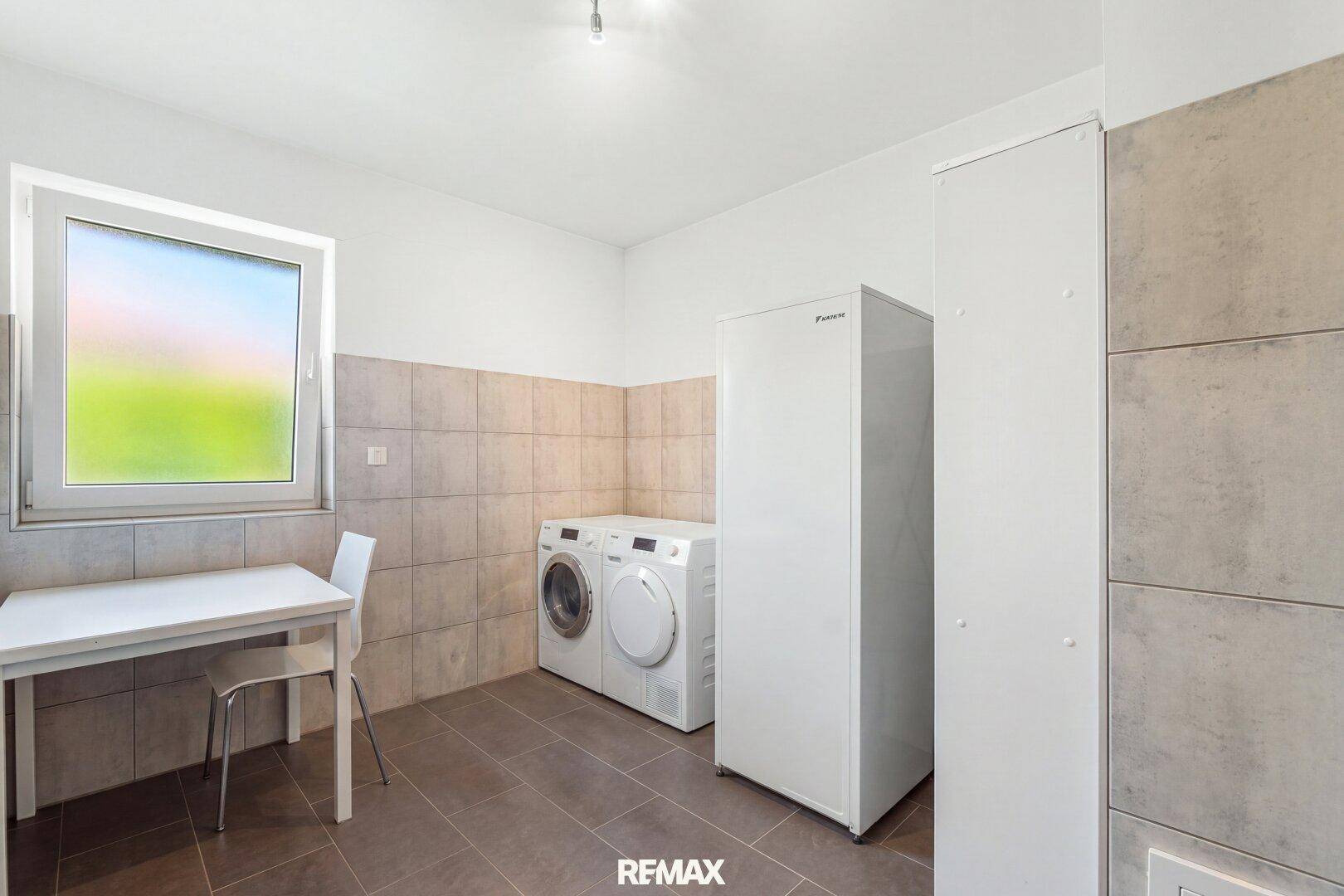 Praktischer Hauswirtschaftsraum mit Waschmaschine, Trockner, Gefrierschrank und Fenster.