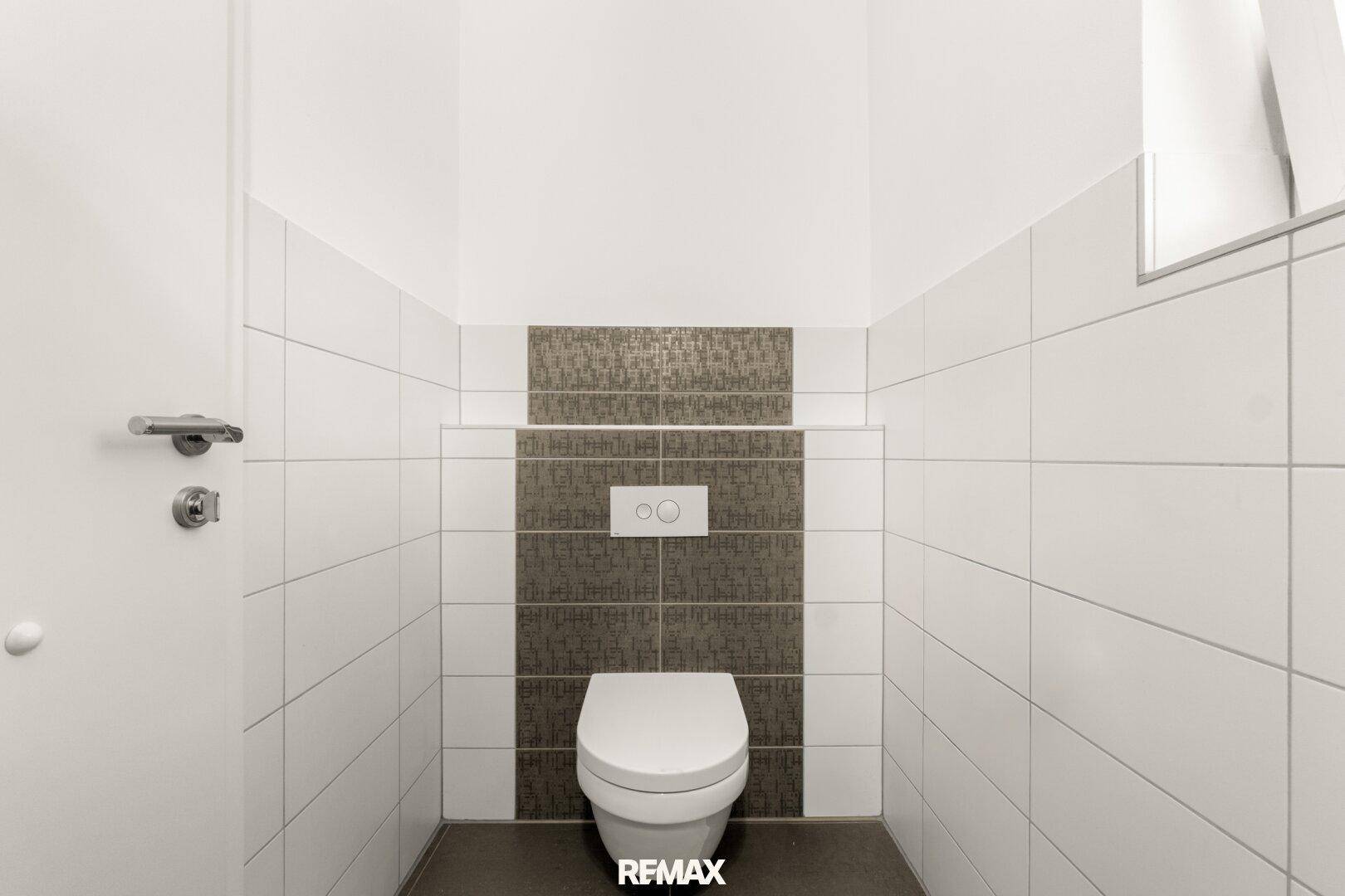Separates WC mit Wand-WC und modernen Fliesen, funktional und sauber gestaltet.