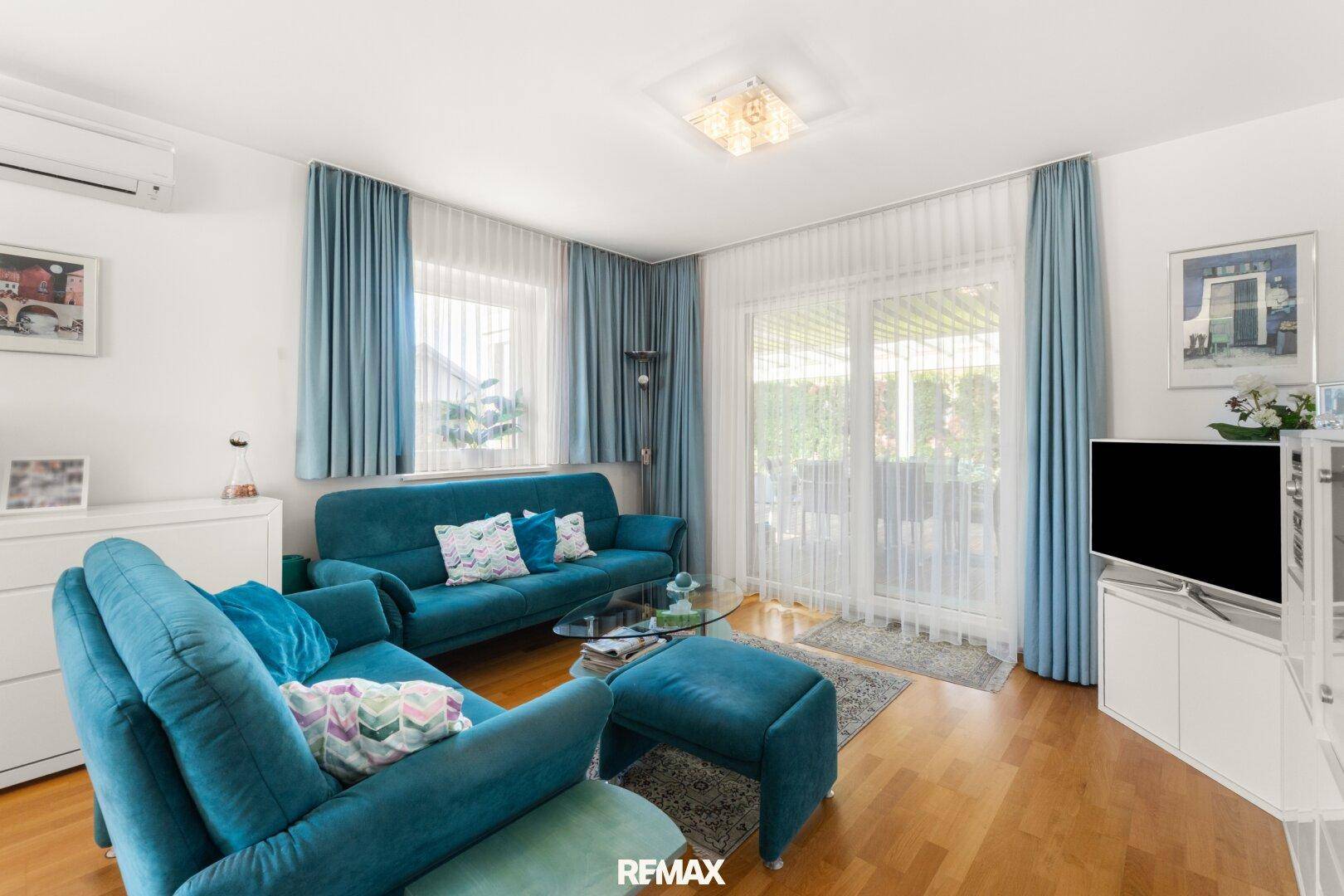 Helles Wohnzimmer mit blauen Sofas, großem Fenster und Zugang zur Terrasse.