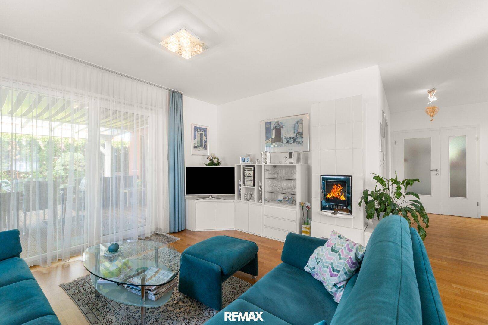 Gemütliches Wohnzimmer mit Kamin, blauen Sofas und direktem Zugang zum Außenbereich.