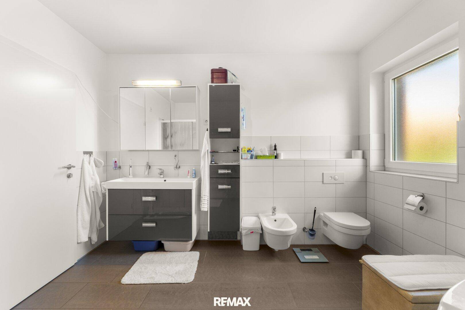 Helles Badezimmer mit modernem Waschtisch, WC, Bidet und Fenster für Tageslicht.