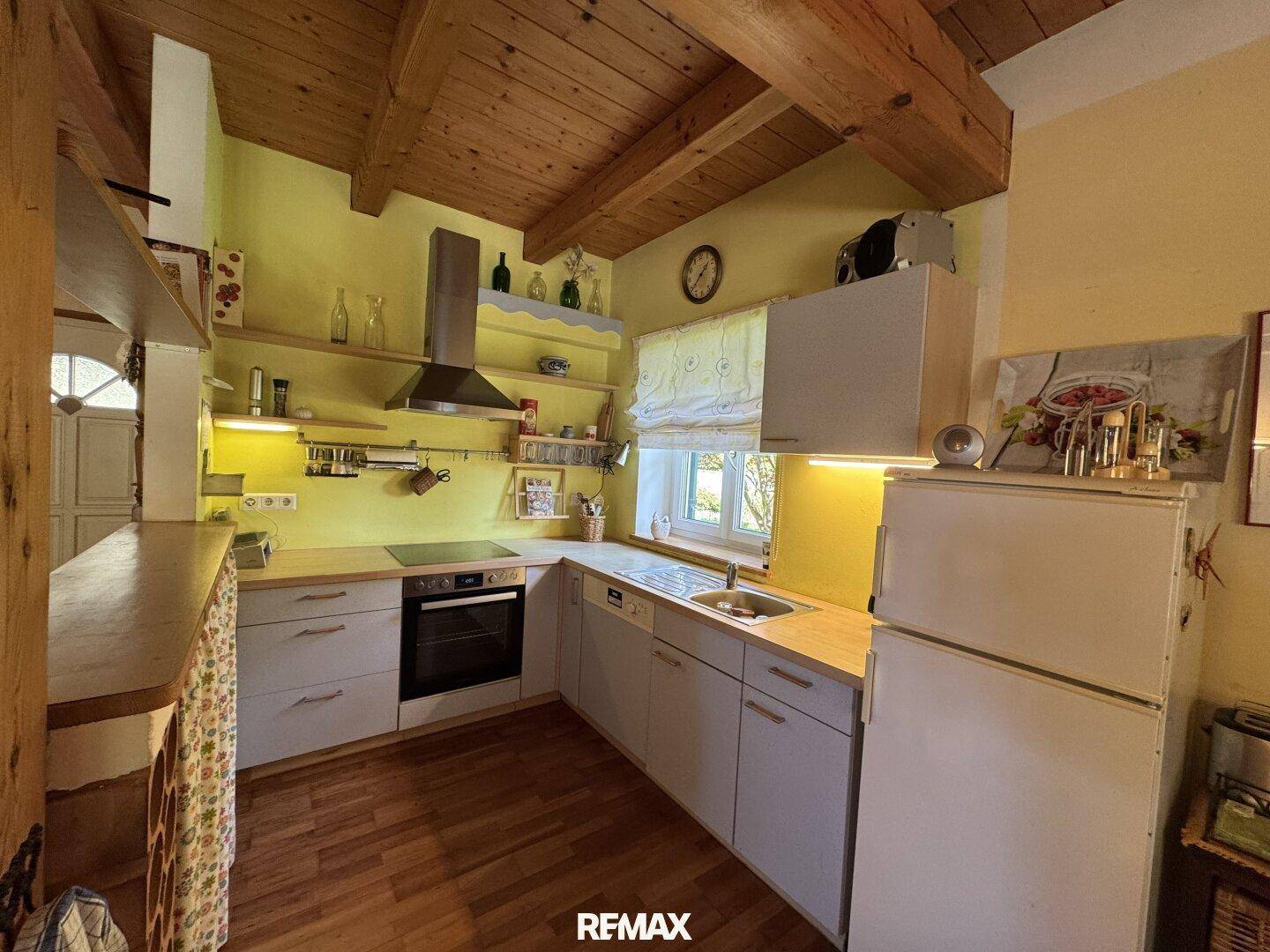 Helle Landhausküche mit Holzbalkendecke, gelben Wänden und Blick ins Grüne.