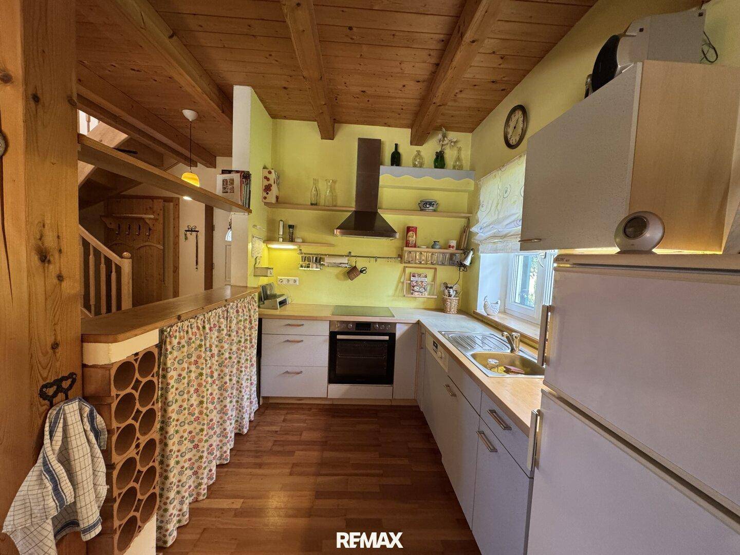 Gemütliche Küche im Landhausstil mit Holzbalkendecke, gelben Wänden und integrierten Geräten.