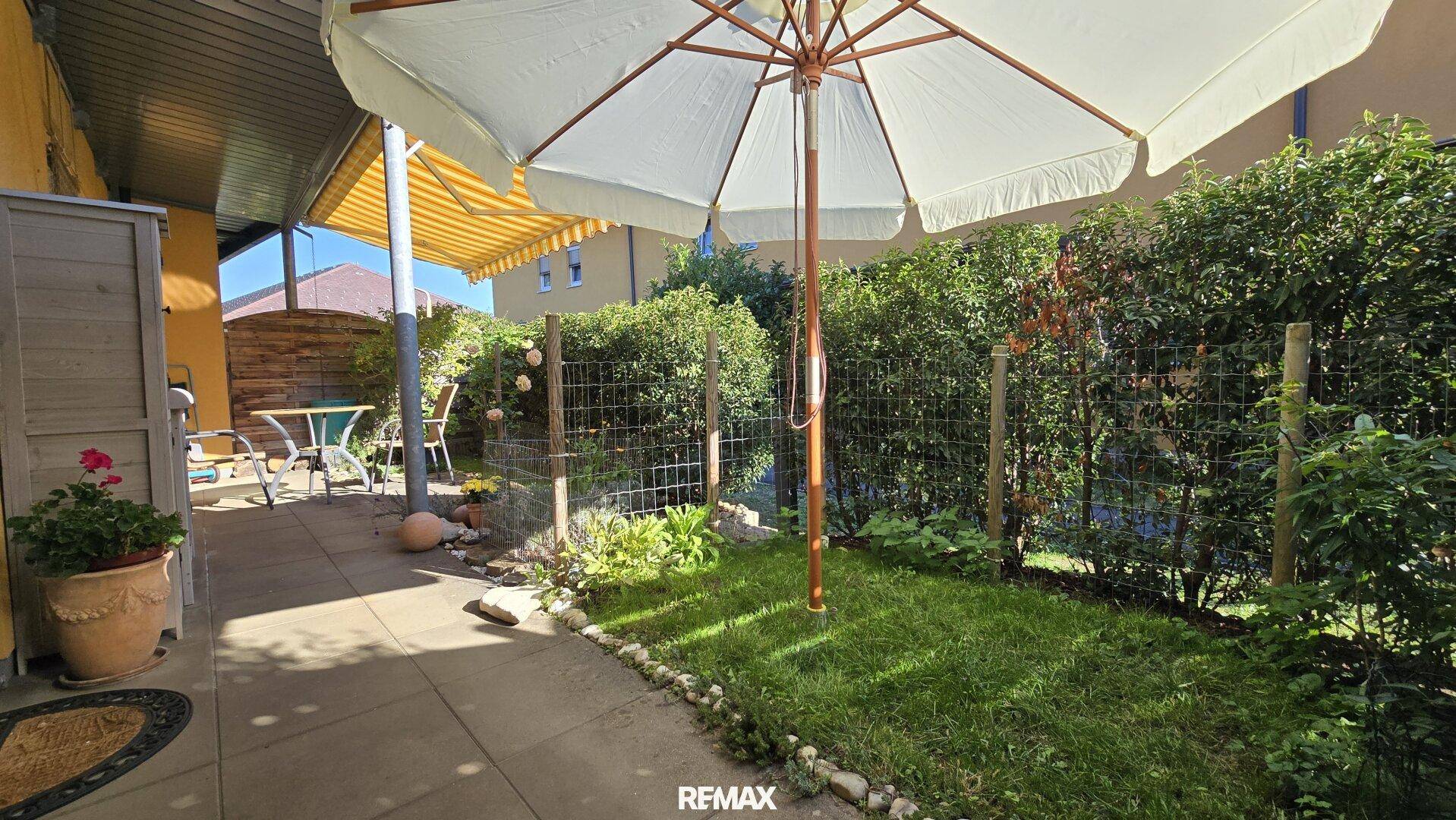 Sonnige Gartenecke mit großem Sonnenschirm, Rasenfläche und gepflegter Hecke, ideal zum Entspannen.