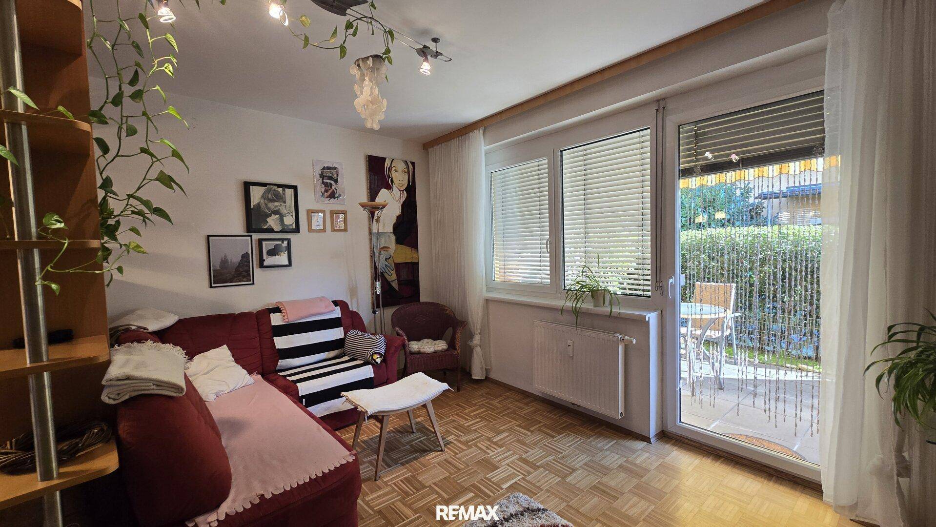 Gemütliches Wohnzimmer mit rotem Sofa, großen Fenstern und direktem Zugang zur sonnigen Terrasse.