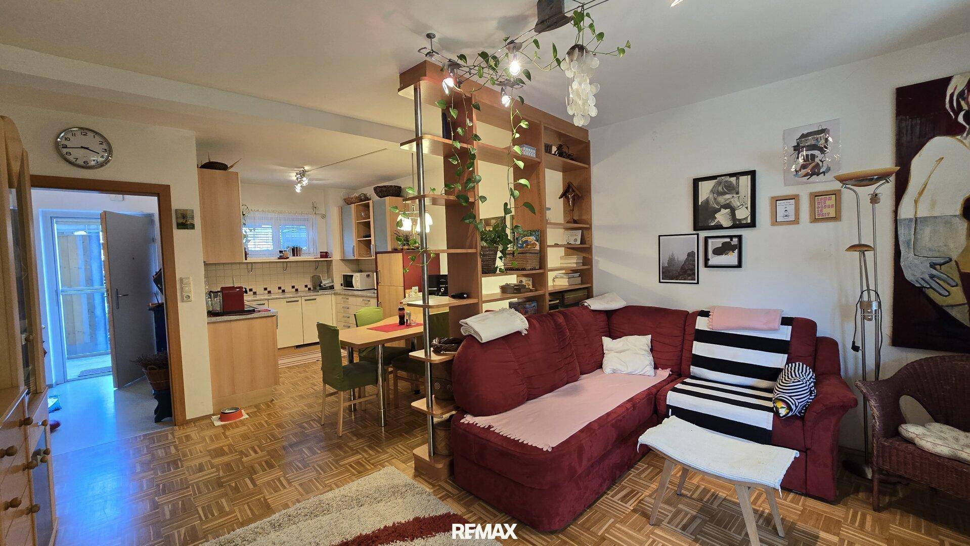 Offener Wohnbereich mit rotem Sofa, Holzregal und direktem Übergang zur Küche und zum Essbereich.