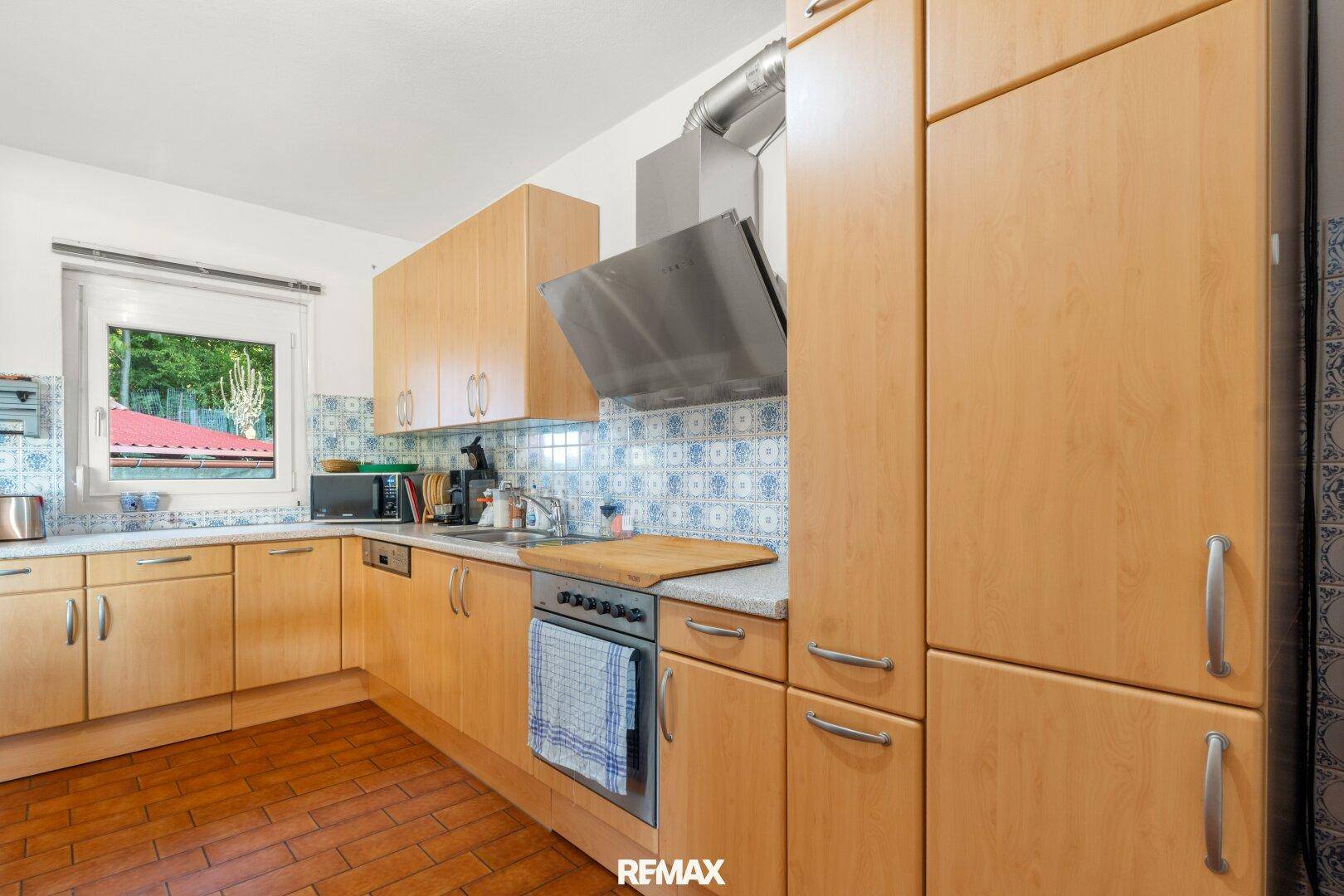 Gut ausgestattete Küche mit Holzfronten, Terrakottafliesen und Fenster für natürliches Licht.