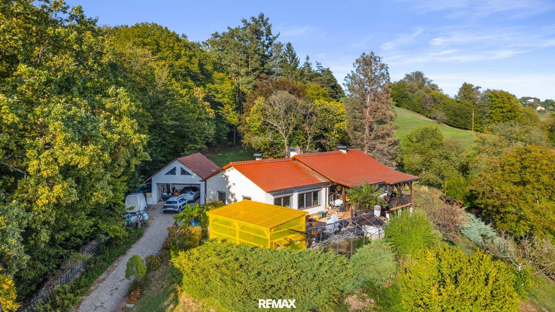 Luftaufnahme des Hauses mit angrenzender Garage und einem überdachten Außenbereich in grüner Umgebung.