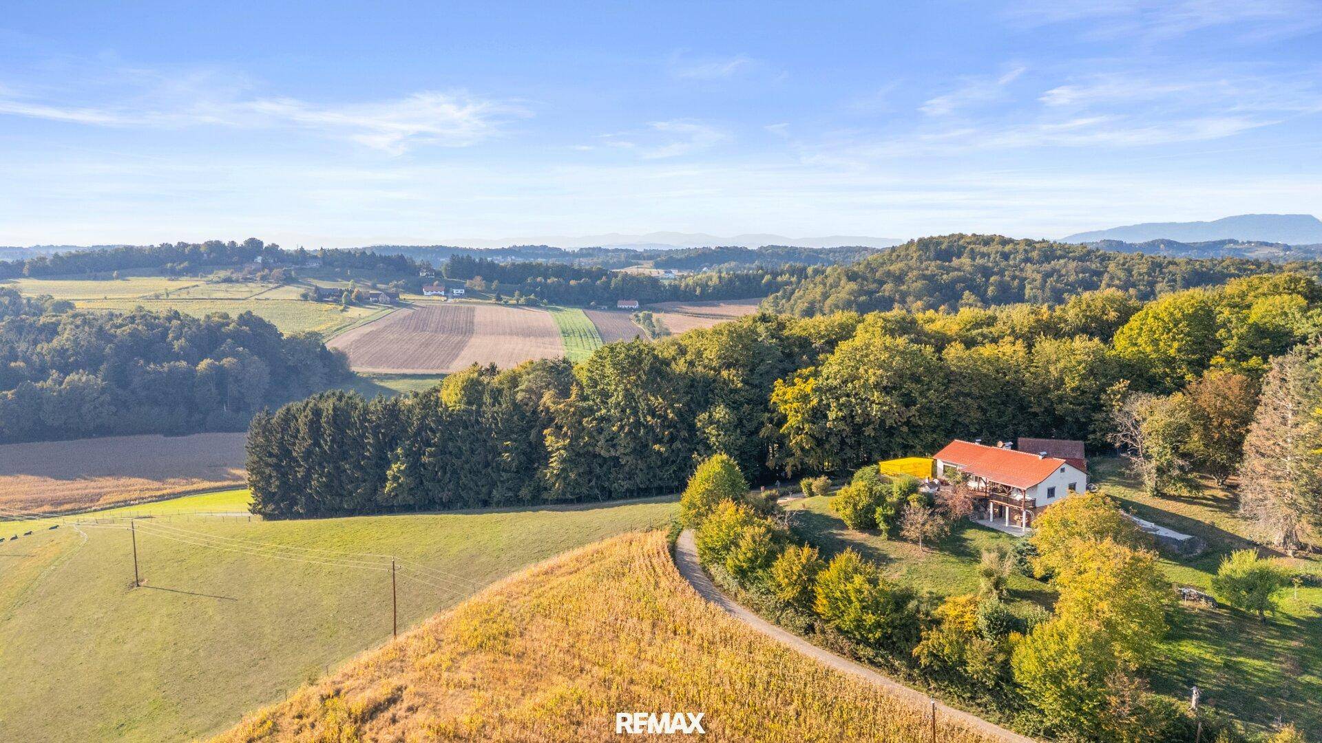 Panoramablick auf das Anwesen mit weiten Feldern und Wäldern unter einem klaren blauen Himmel.