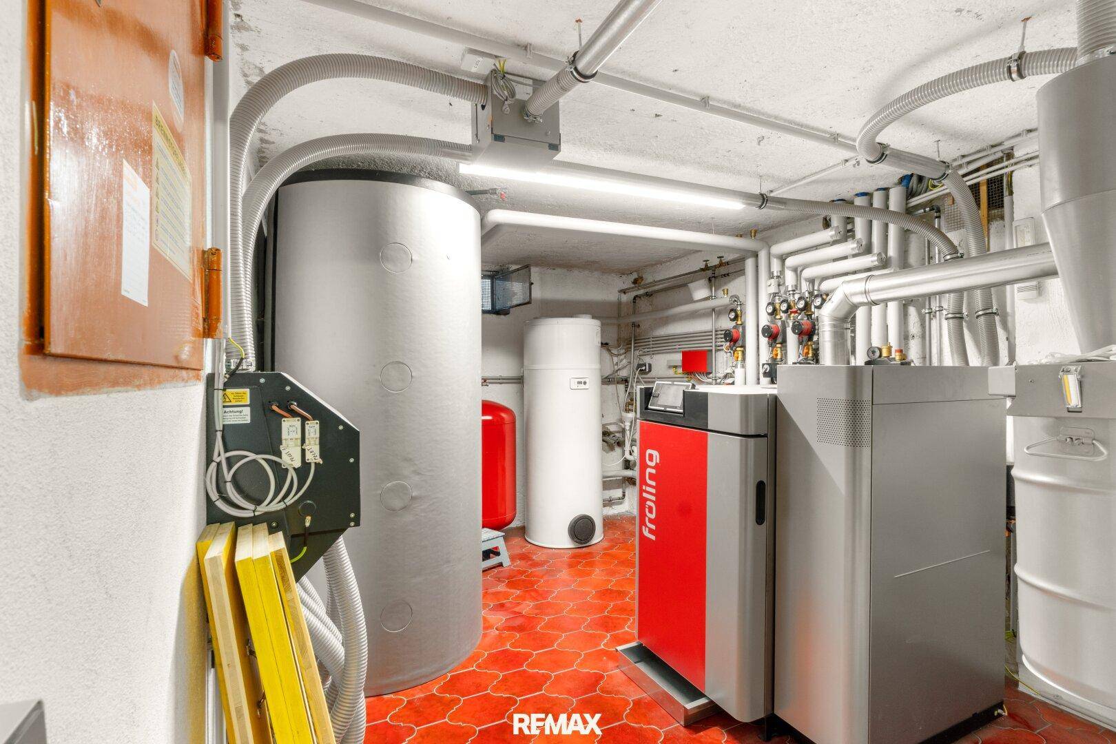 Technikraum im Keller mit moderner Heizungsanlage und Warmwasserspeichern auf Fliesenboden.