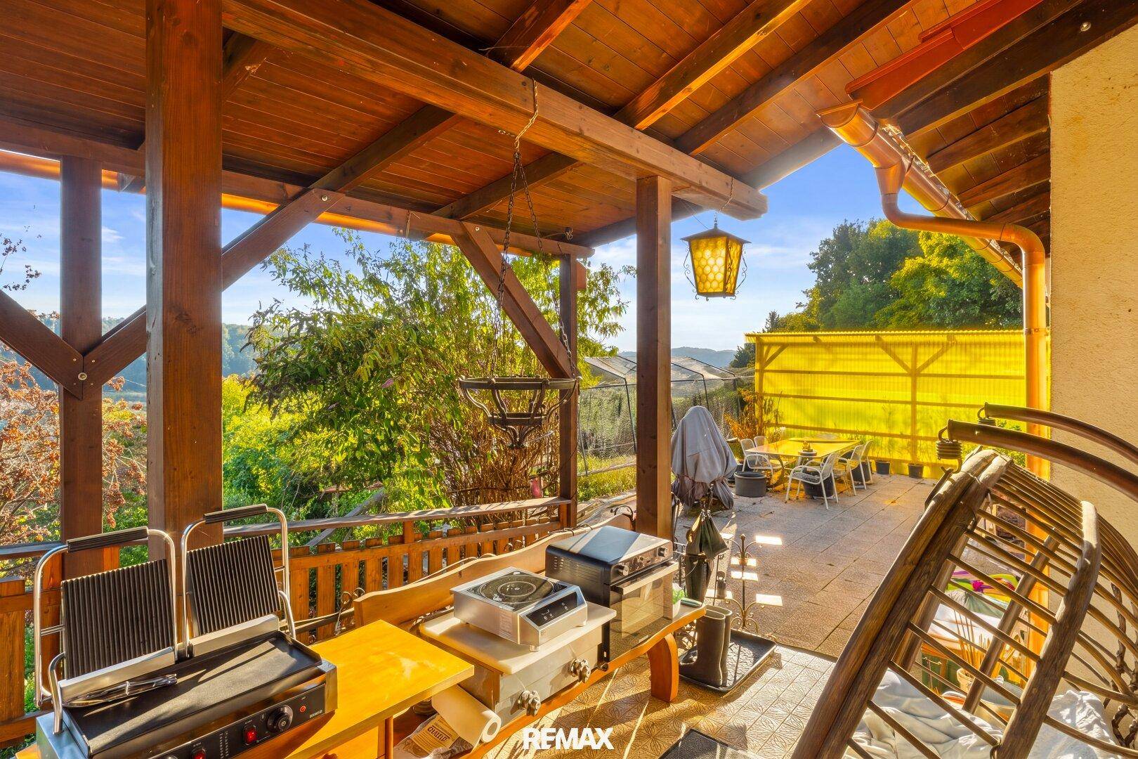 Geräumige überdachte Terrasse mit Grillgeräten und Sitzgelegenheiten, ideal für Mahlzeiten im Freien.