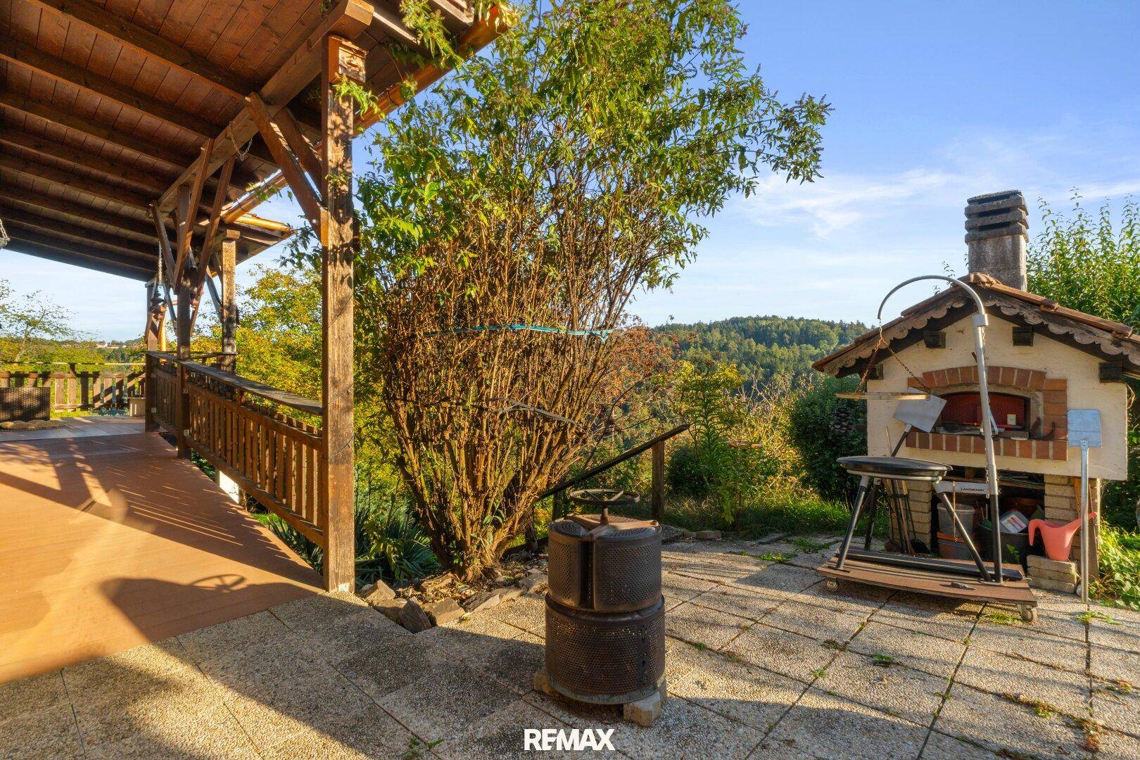 Überdachte Terrasse mit rustikalem Pizzaofen und weitem Blick auf die umliegende Landschaft.