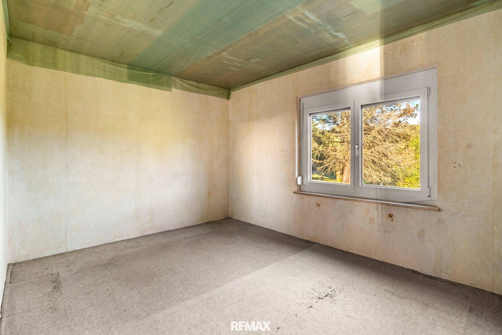 Leerer Raum mit Betonboden und Fenster, der auf eine Renovierung wartet.