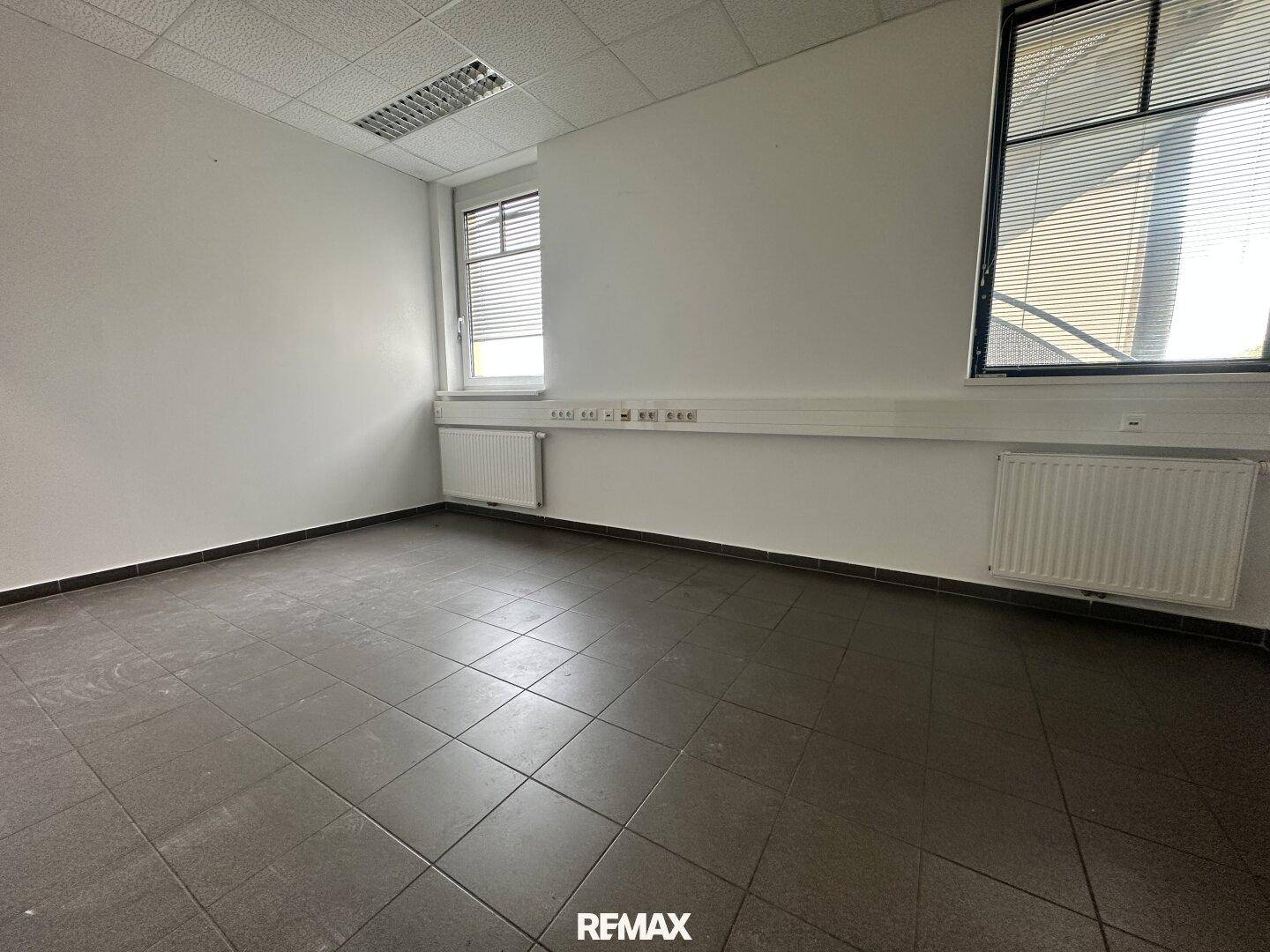 Leeres Büro mit grauen Fliesen, weißen Wänden und Deckenplatten, bereit zur Einrichtung.