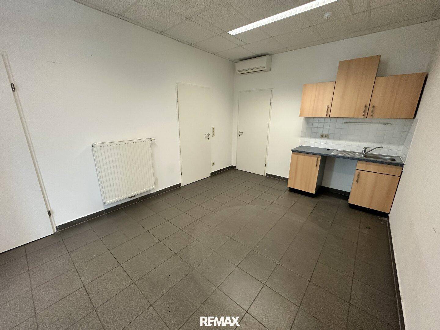 Bürofläche mit integrierter Küchenzeile, Heizkörper und Deckenbeleuchtung, funktional eingerichtet.