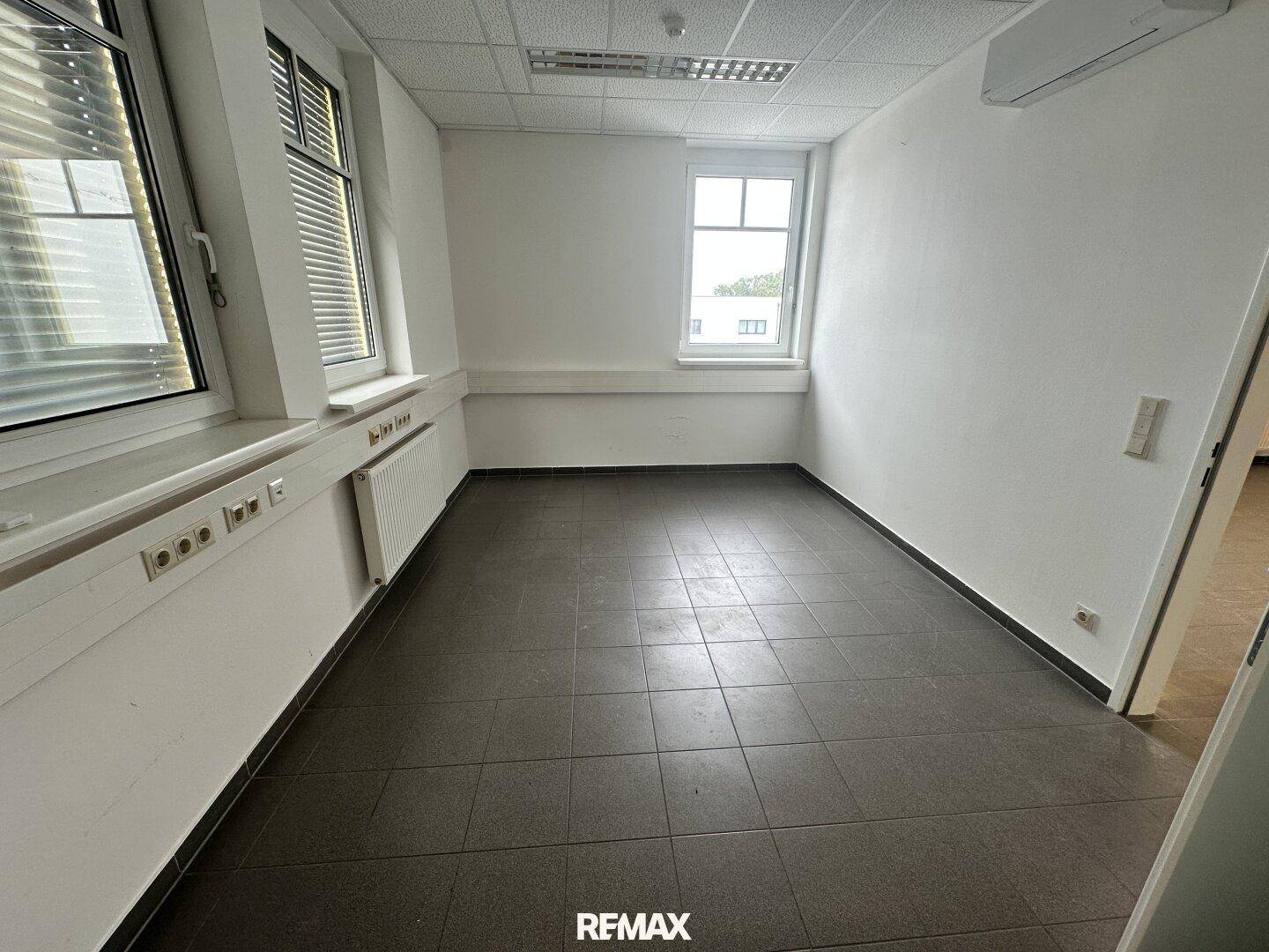 Helles Büro mit Fliesenboden und zwei Fenstern, bietet viel Tageslicht für eine angenehme Arbeitsatmosphäre.