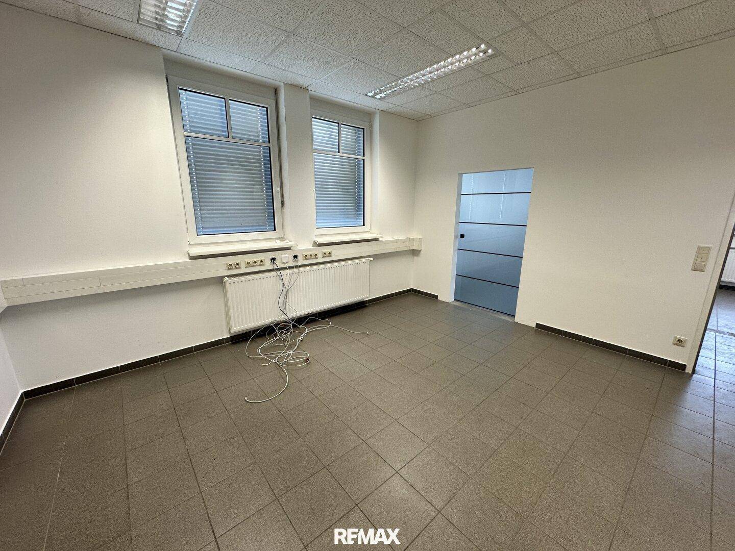 Modernes Büro mit Fliesenboden, großen Fenstern und einer Glastür, ideal für flexible Arbeitsbereiche.