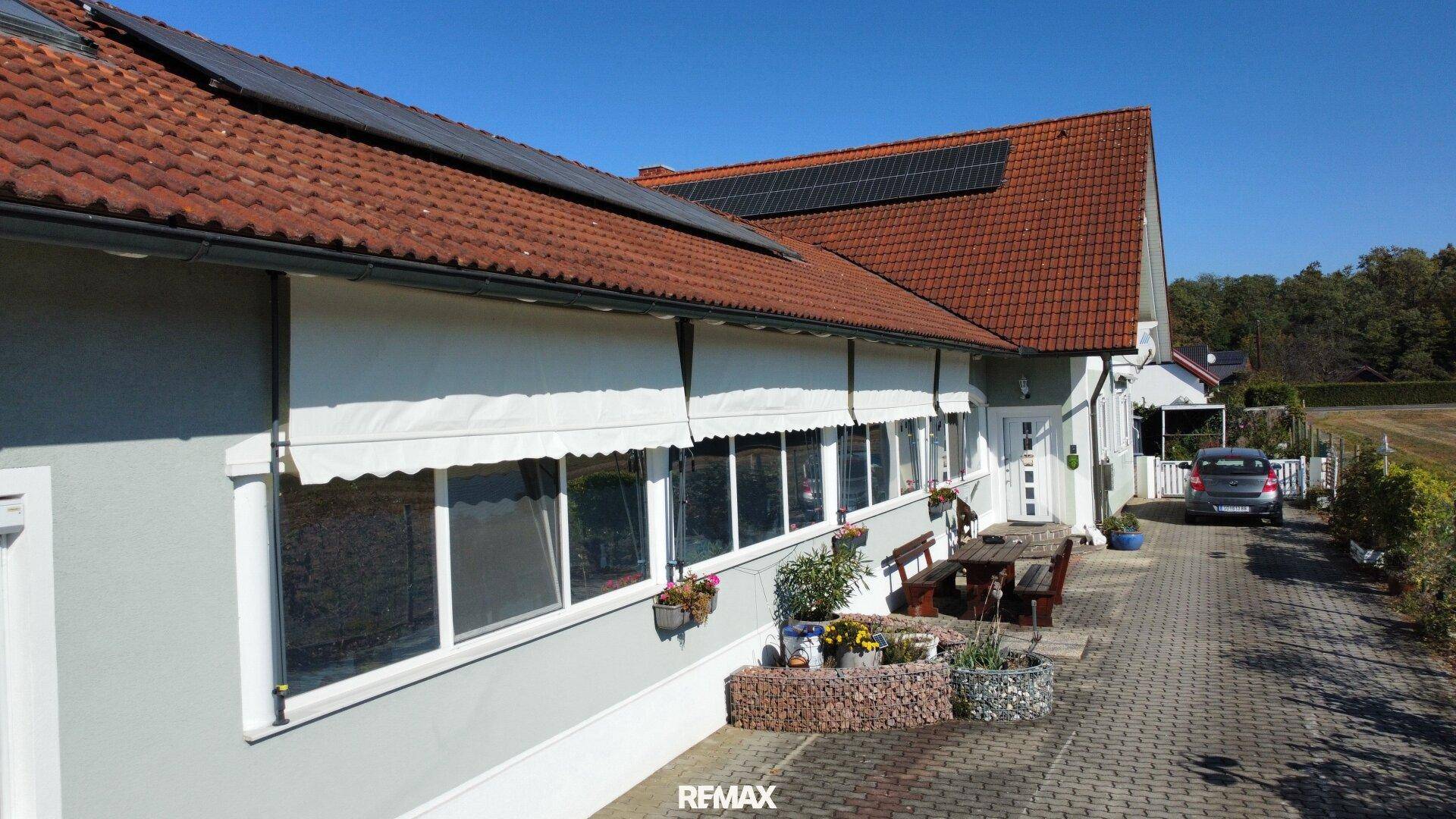 Seitenansicht des Hauses mit Photovoltaikanlage, Markisen und gepflastertem Vorplatz.