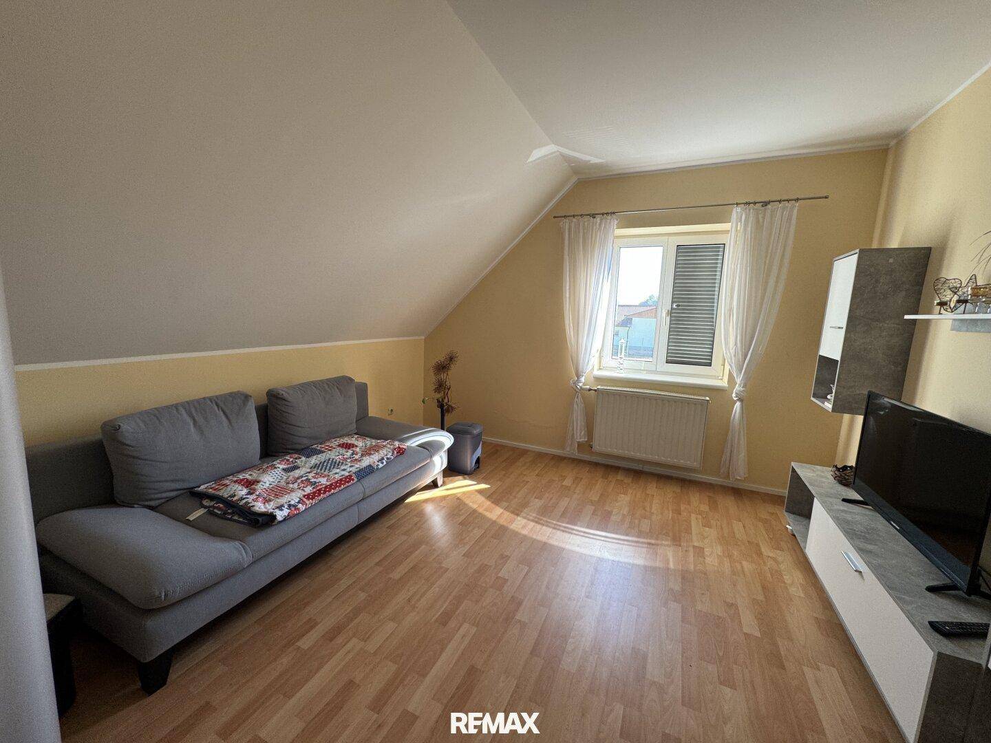 Helles Wohnzimmer im Dachgeschoss mit Sofa, TV-Möbeln und Laminatboden.