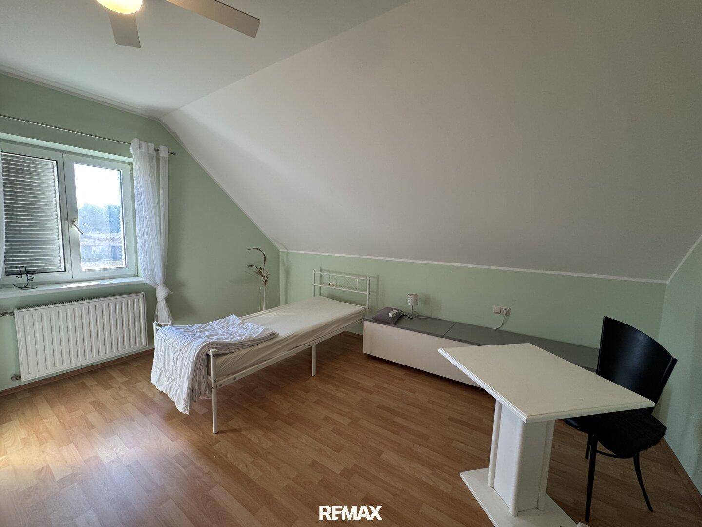 Schlafzimmer im Dachgeschoss mit Einzelbett, Schreibtisch und Laminatboden.