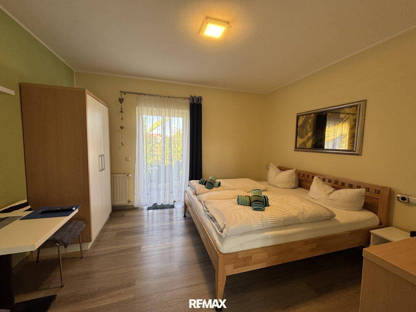 Helles Schlafzimmer mit zwei Einzelbetten, Kleiderschrank und Zugang zu einem Balkon.