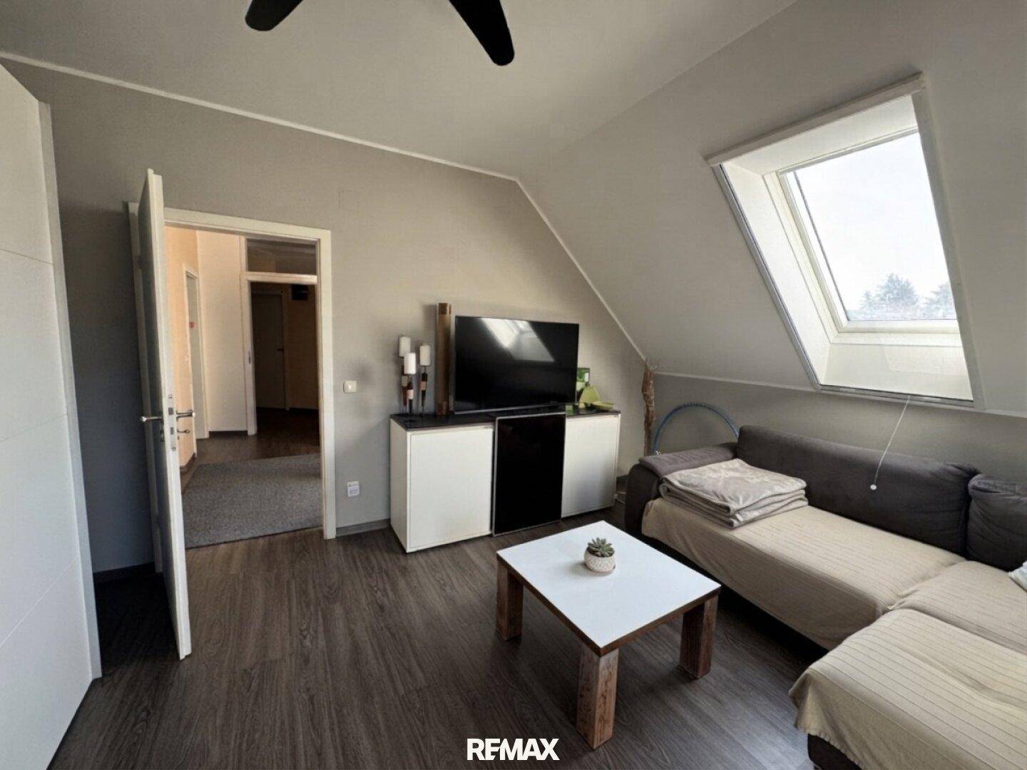 Wohnzimmer im Dachgeschoss mit Sofa, TV-Möbeln und Zugang zum Flur.