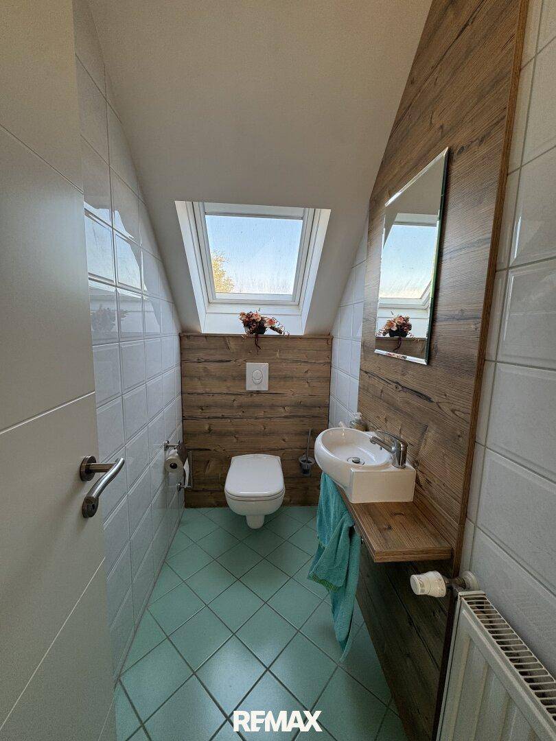 Kleines WC mit Toilette, Waschbecken und Dachfenster, Holzakzente an der Wand.