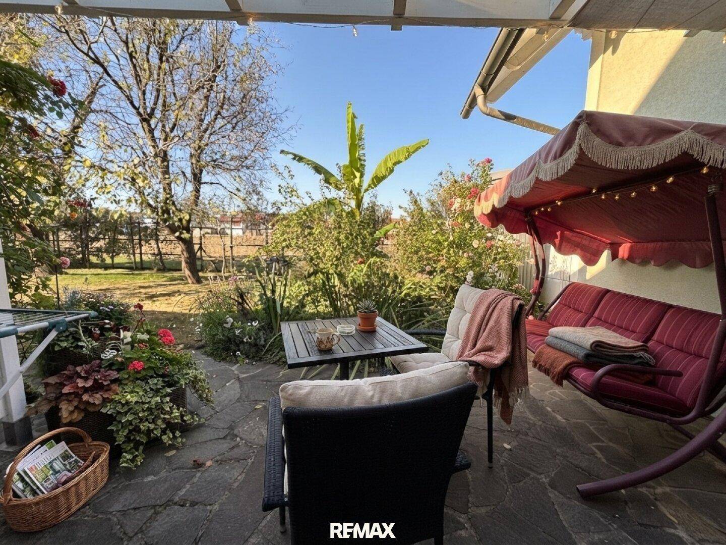 Einladende Terrasse mit Gartenmöbeln und Schaukel, umgeben von üppigem Grün.