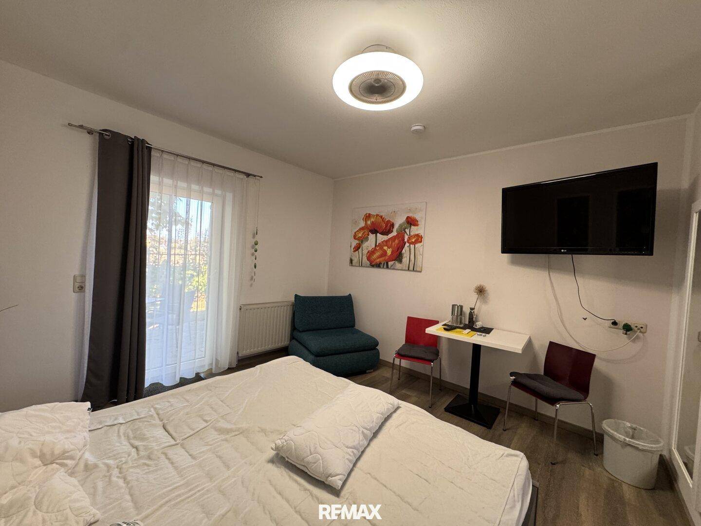 Helles Schlafzimmer mit Doppelbett, kleinem Tisch und Zugang zu einem Balkon.