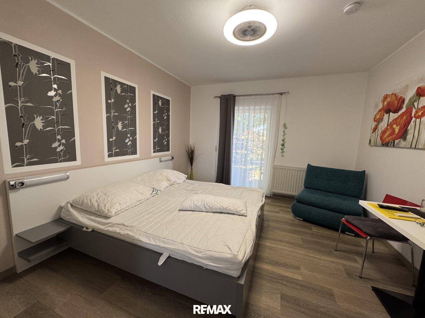 Schlafzimmer mit Doppelbett, Sitzgelegenheit und Balkonzugang, dekoriert mit Wandbildern.