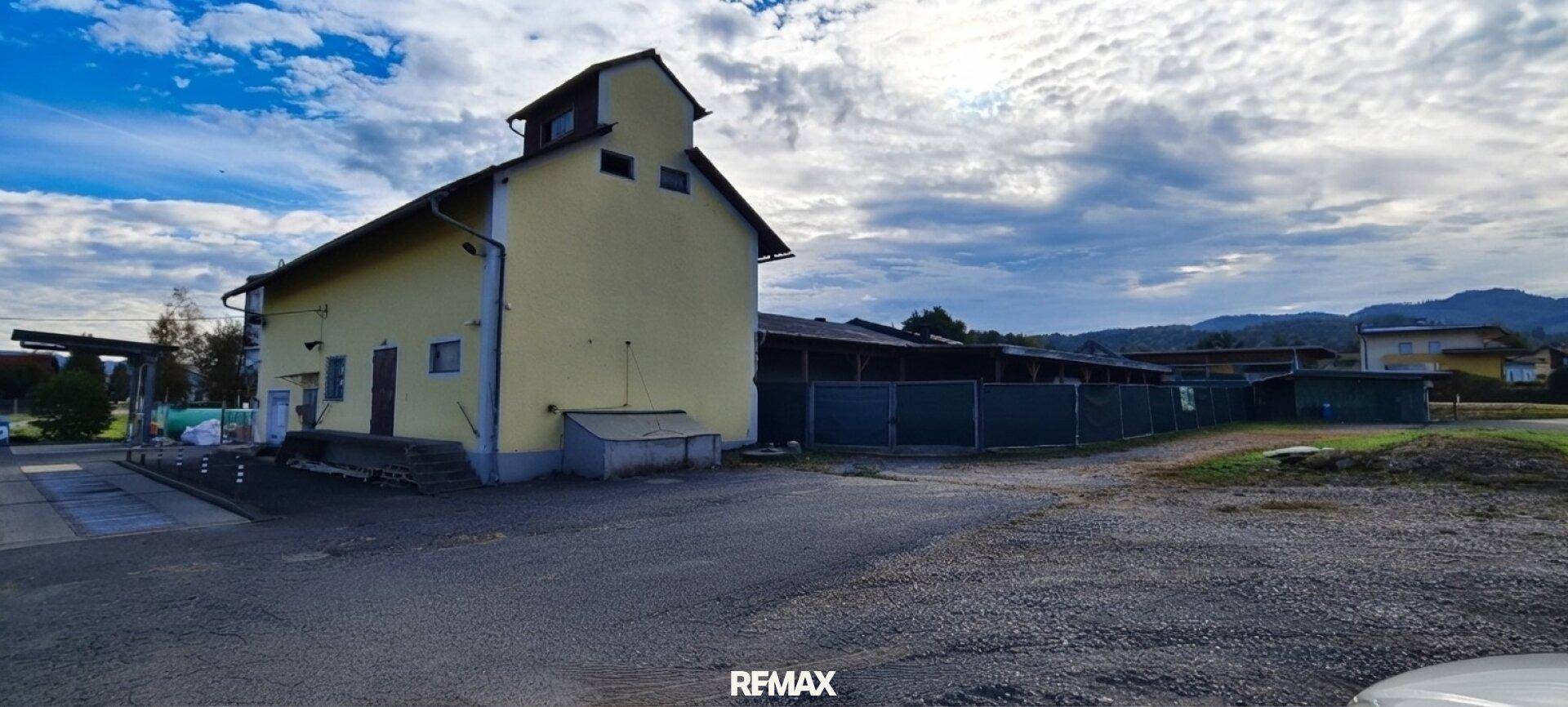 Gelbes Gebäude mit großem Vorplatz und weitem Himmel, umgeben von ländlicher Landschaft.