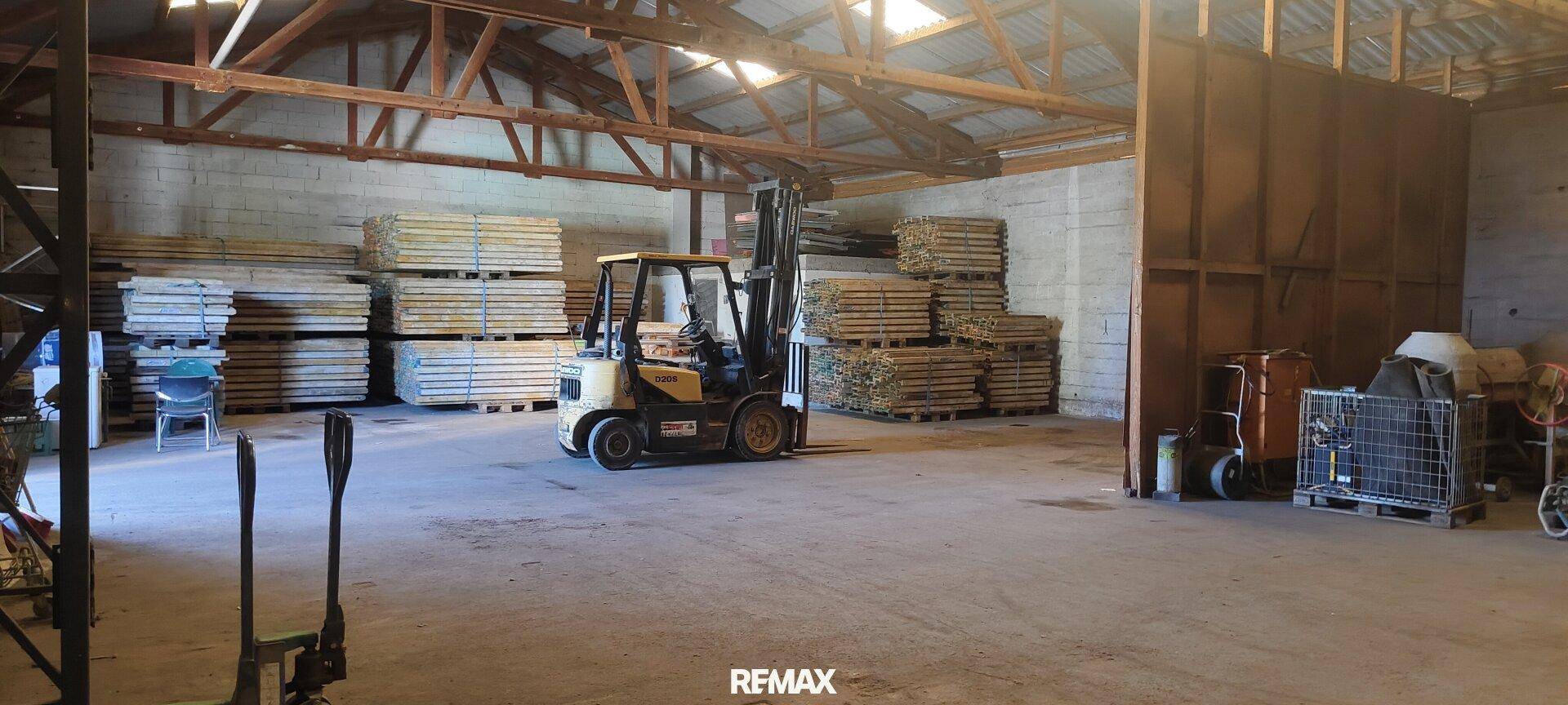 Weitläufiger Lagerraum mit Gabelstapler und gestapeltem Holz, unter Holzdachkonstruktion.