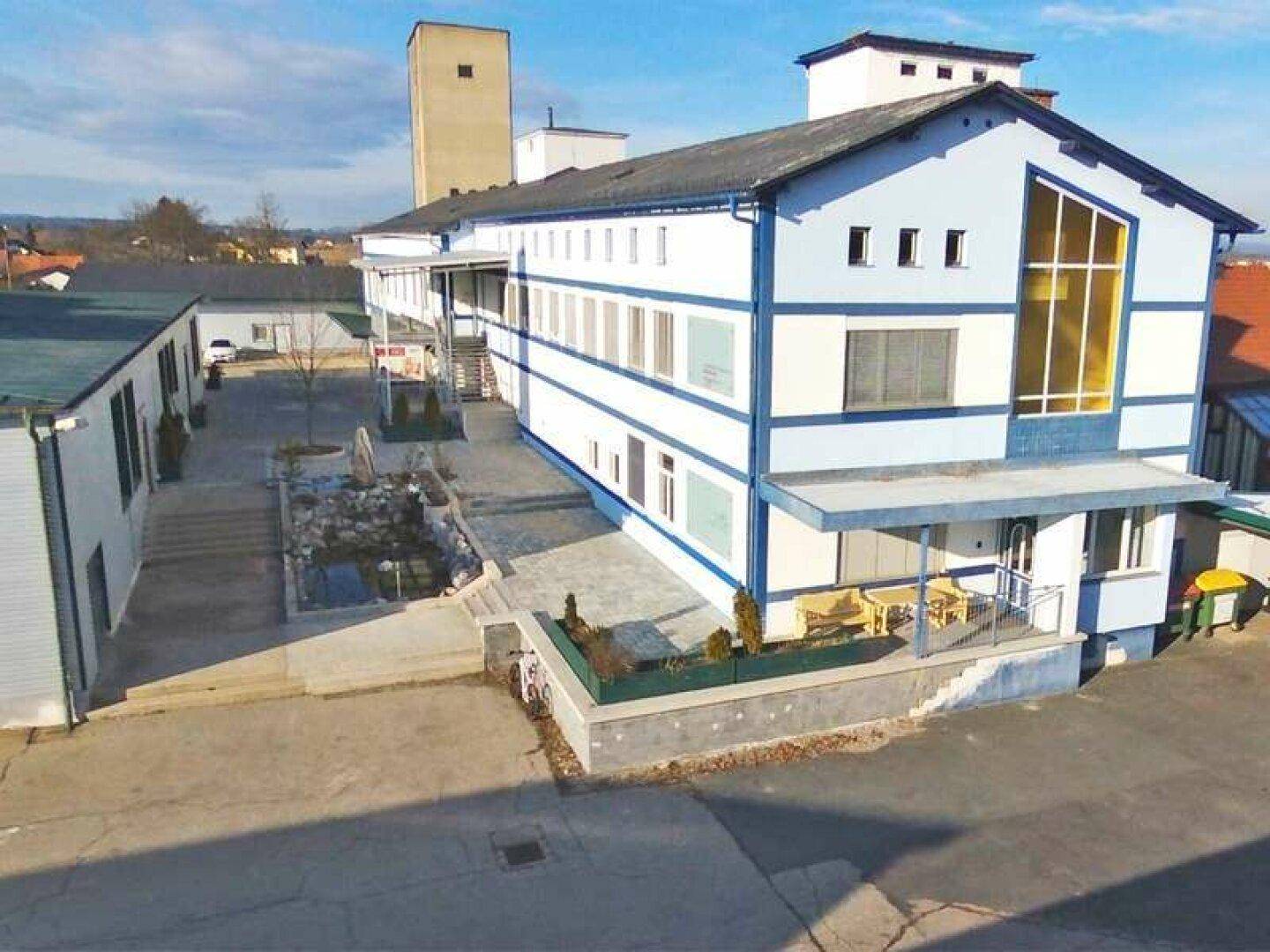 Ansicht des modernen Gebäudes mit blauen Akzenten, großen Fenstern und einem gepflasterten Vorplatz.
