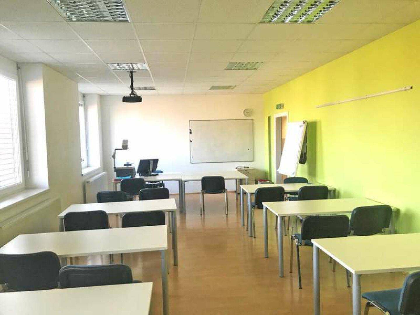 Geräumiger Schulungsraum mit Tischen, Stühlen, Whiteboard und einem Deckenprojektor für interaktive Lektionen.